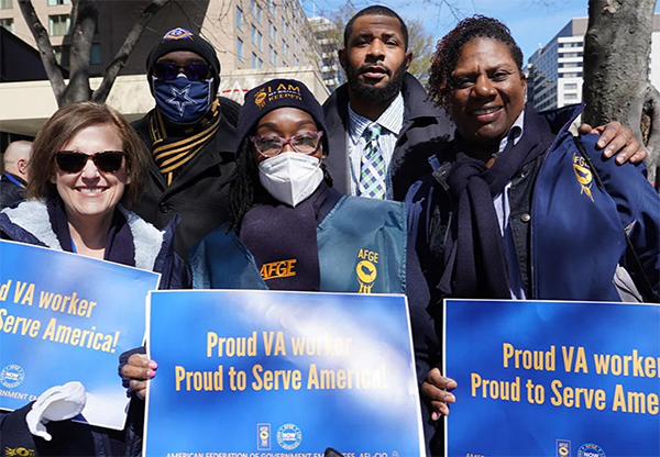 AFGE members pose for a group picture with signs that read, "Proud VA worker. Proud to serve America."