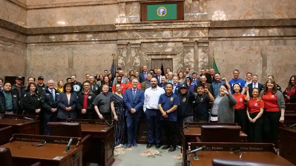 Workers posing for group photos with lawmakers in the Washington State Legislature Senate chambers.